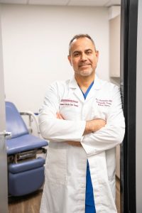 Man in white coat leaning against a wall smiling