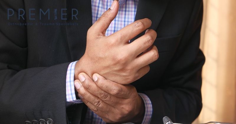 Man with Black Suit Jacket and Pink and Blue Button Down Shirt Holding His Wrist