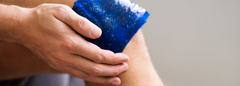 oung man holds cold pack on knee to treat a sports-injury at home with recommendations for the orthopedic surgeons at Premier Orthopaedic & Trauma Specialists