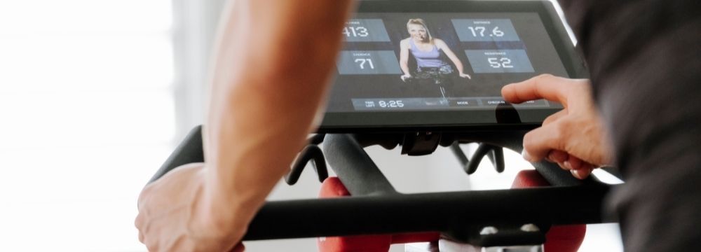 Woman rides stationary bike to receive the benefits of cardio and resistance training for her overall and orthopedic health according to recommendations by experts at Premier Orthopaedics & Trauma Specialists 