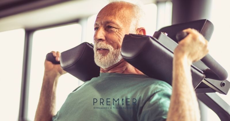 Older man exercises using weight bearing activities to improve strength and bone heath as instructed by his orthopedic surgeon. Premier Ortho logo at bottom center. 